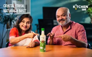 A happy couple sitting at a kitchen table pointing to a bottle of Kitchen Soul organic cooking oil, promoting its crystal-fresh and natural quality.